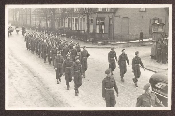 Black and white photo of Dutch soldiers marching in formation through a village street