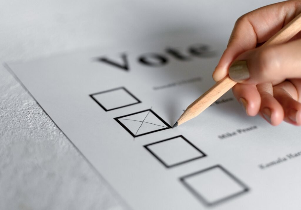 Close-up of hand marking a checkbox on a voting ballot with a pencil
