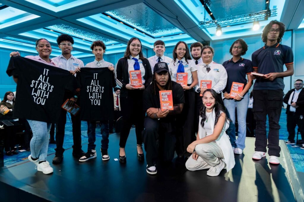 Group of Aruba students with Trent Shelton holding “Protect Your Peace” books and “It All Starts With You” t-shirts at Voices of Tourism.