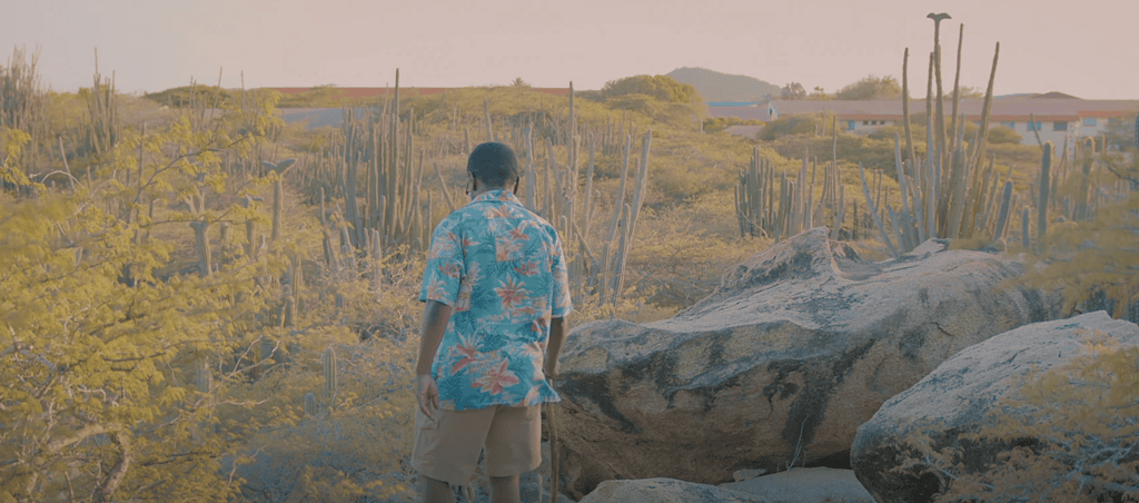 Modern photo of a man in Aruba walking toward a large cross on a hill at Canashito in Santa Cruz, reflecting Spanish colonial religious influence.
