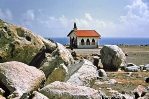 Landscape photo of Alto Vista Chapel in Aruba overlooking the Caribbean Sea, surrounded by cactus and rocks.