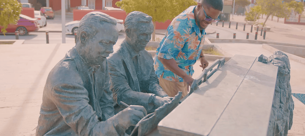 Statue of Rufo Wever and Juan Chabaya Lampe, composers of Aruba’s national anthem, with a visitor interacting at the piano monument in Oranjestad.