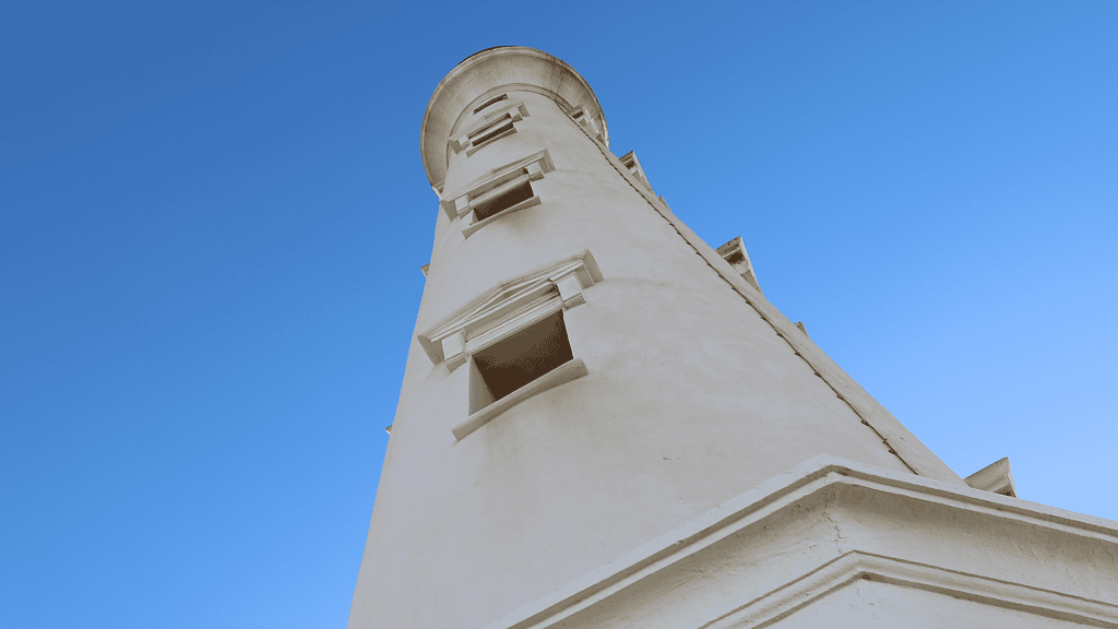 Historic lighthouse with white exterior and blue sky background, belonging to Djis Pa Hari, showcasing coastal navigation and maritime safety.