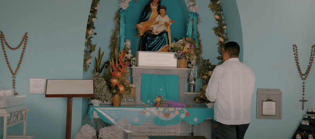 Devotee praying inside the modern Alto Vista Chapel in Aruba in front of the Virgin Mary statue.