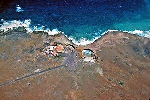 Secluded coastal retreat on a rugged shoreline with a natural arch, overlooking the ocean; perfect for a peaceful getaway or a unique event location.