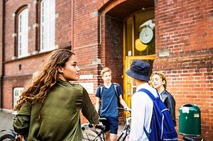 School students standing and talking outside brick school building with bicycles in the background, young people, education, student life, peer interaction, urban school setting.