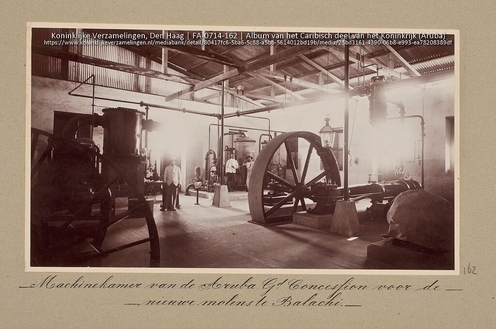 Steam engine room in Curacao used for the new mills at Balachi, vintage black and white photograph of industrial machinery, historical steam-powered equipment, and workers in early 20th-century industry.