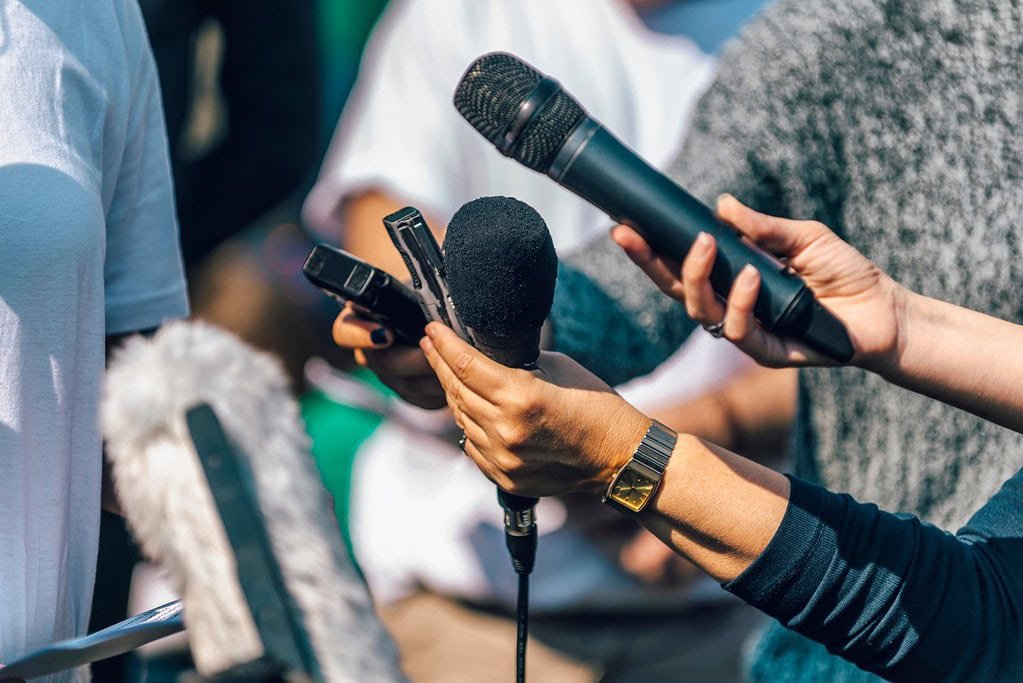 Microphone and voice recorder being held during an interview or press conference, capturing audio for media coverage or communication purposes.